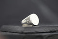 Silver signet ring with intricate side engravings on a dark surface.