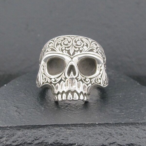 Intricately designed silver skull ring with detailed carvings.