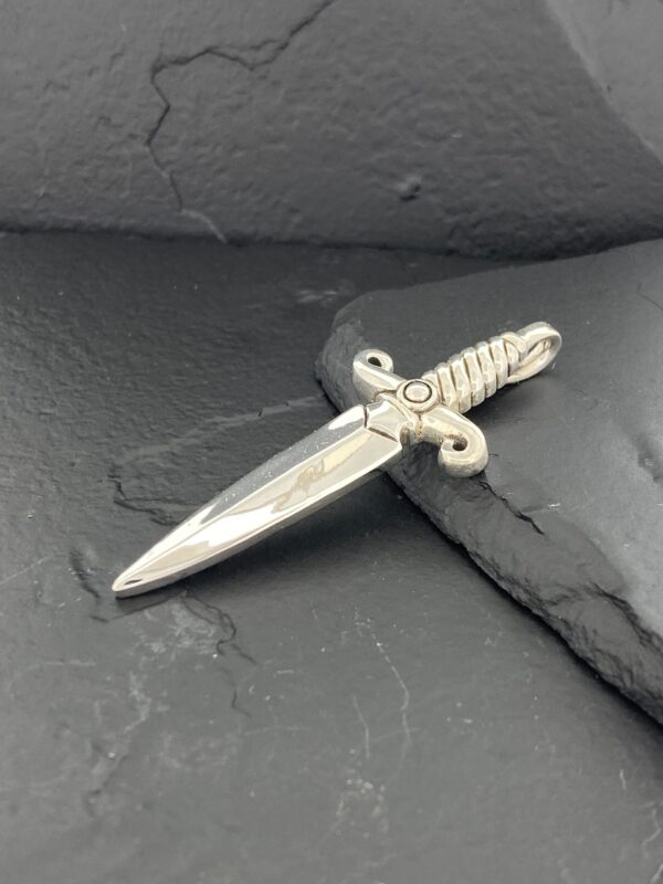 A small dagger-shaped pendant with a twisted handle on a dark surface.