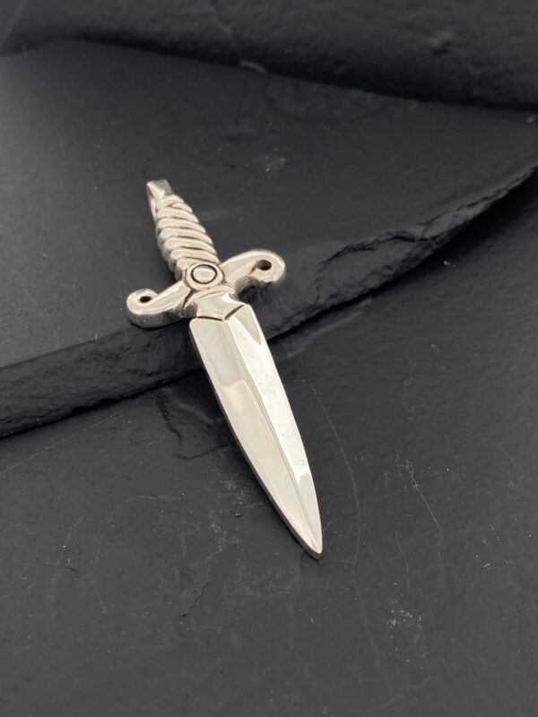 A silver dagger pendant with intricate handle details on a dark background.
