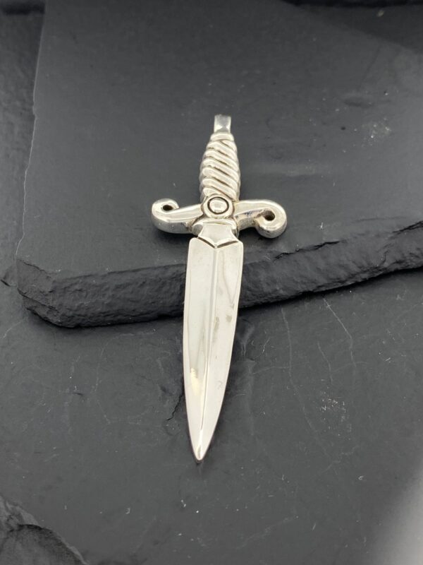 Ornate silver dagger pendant with a detailed hilt on a dark slate background.