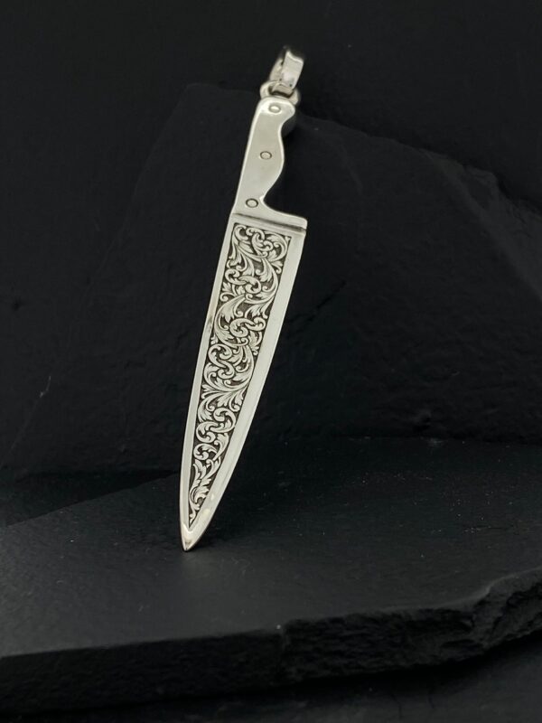 A silver knife-shaped pendant with intricate floral engravings.