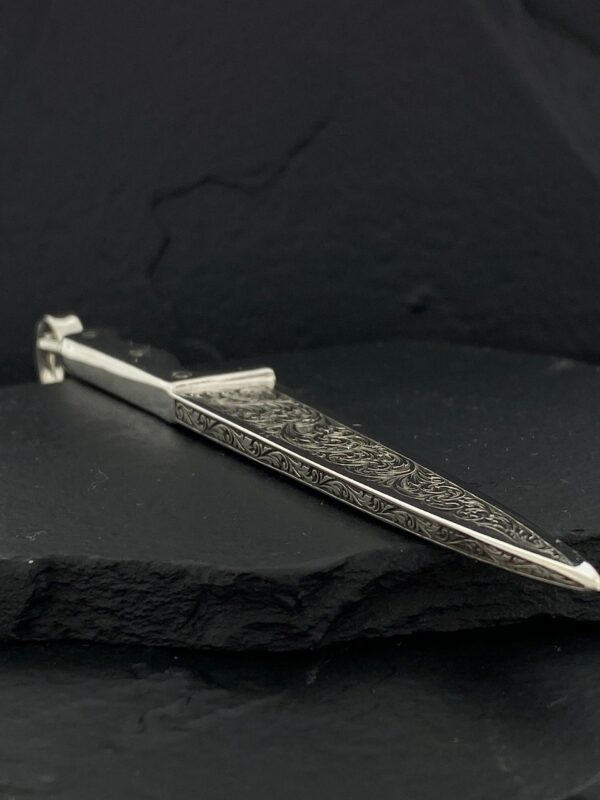 Elegant silver tie clip with textured design on a dark background.