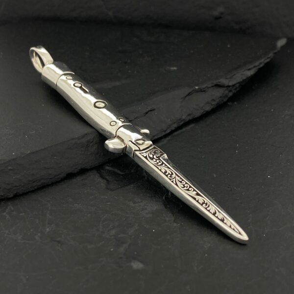 Silver dagger-shaped pendant with intricate detailing on a dark background.