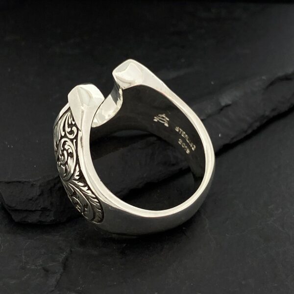 Silver ring with intricate leaf and vine design on a black background.