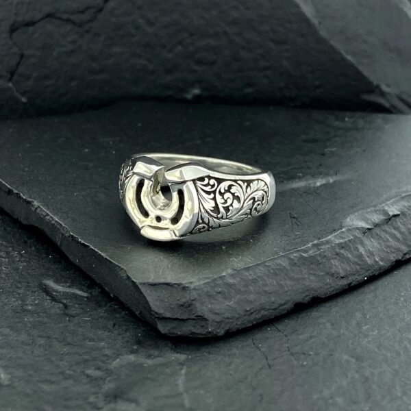 Close-up of a detailed silver ring on a dark stone surface.