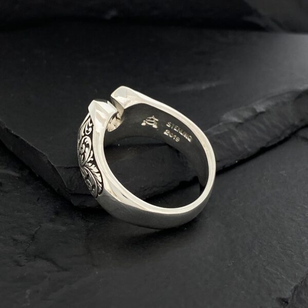 Close-up of a detailed silver ring on a black surface.