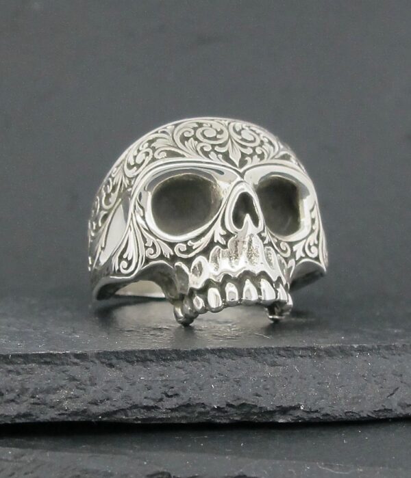 Intricately detailed silver skull ring with ornate patterns.
