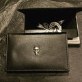 Black leather wallet with a skull emblem and a box in the background.