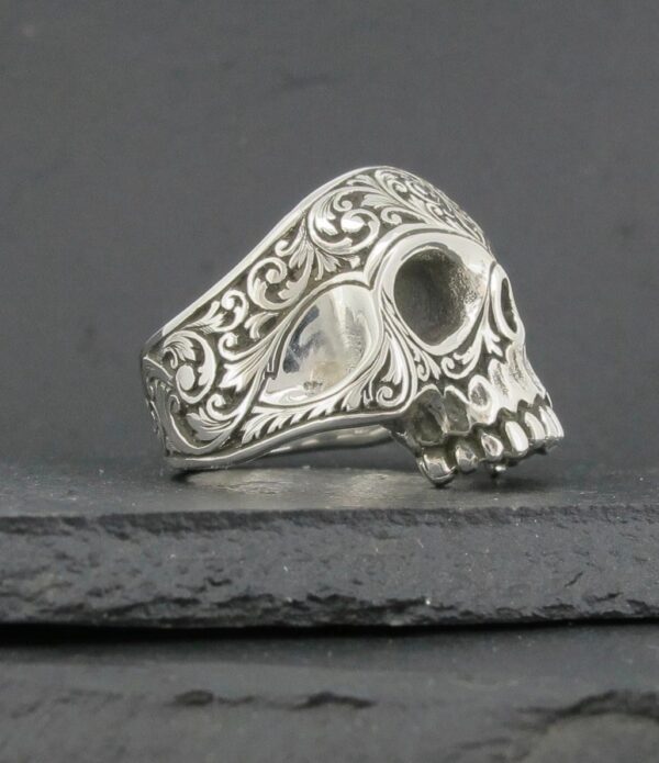 Ornate silver skull ring with intricate floral engravings.
