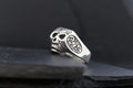 A silver skull ring with intricate engravings on a dark background.