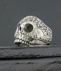 Intricately designed silver skull ring with ornate patterns.