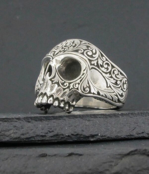 Intricately designed silver skull ring with ornate patterns.