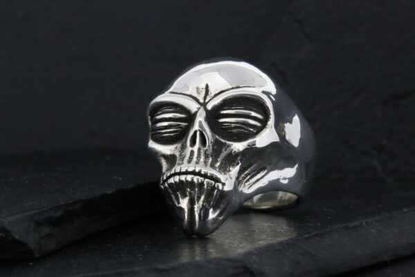 A metallic skull ring with intricate details on a dark background.