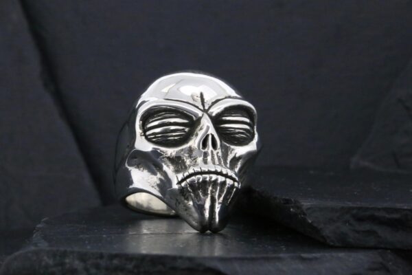 A metallic skull ring with intricate details against a dark background.