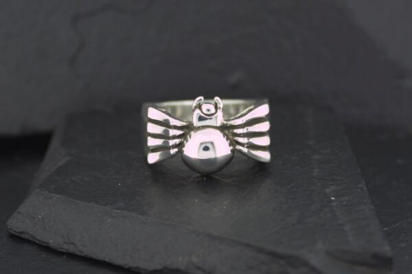 Silver bird-shaped ring with detailed wings on a black surface.