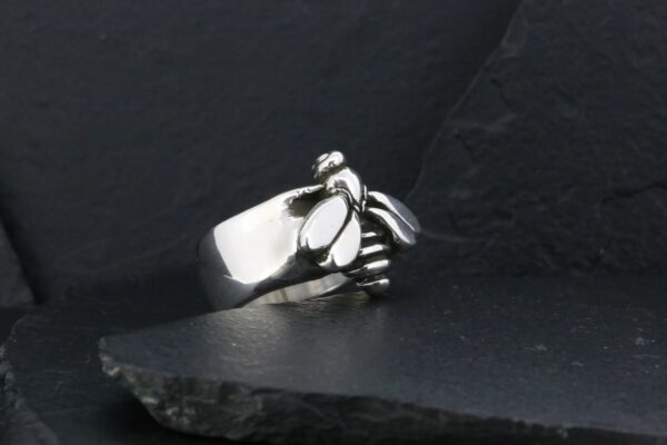 Silver ring shaped like a clenched fist on dark surface.