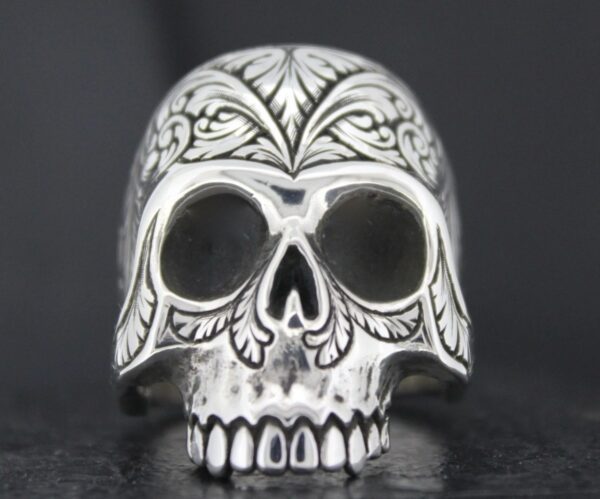 Intricately carved silver skull ring with floral and leaf patterns.