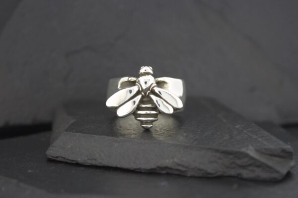 A silver bee-shaped ring on a dark stone surface.