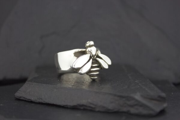 Silver bee-shaped ring on a dark surface.