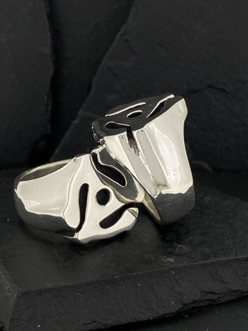Glossy silver rings with unique abstract black designs on a black background.