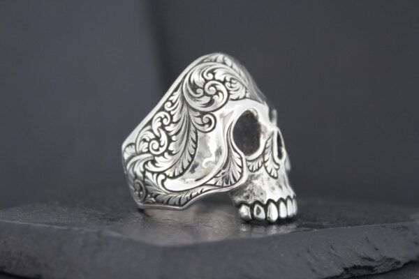 Ornate silver skull ring with intricate engravings.