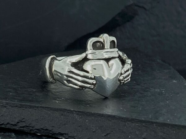 A silver ring with two hands holding a heart.