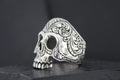 Intricately designed silver skull ring with ornate patterns.