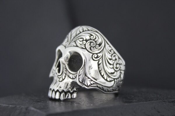 Intricately designed silver skull ring with ornate patterns.