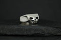 Silver skull-shaped ring on a dark surface.
