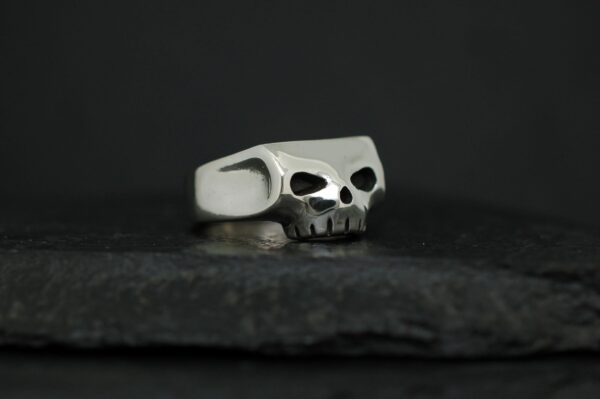 Silver skull-shaped ring on a dark surface.