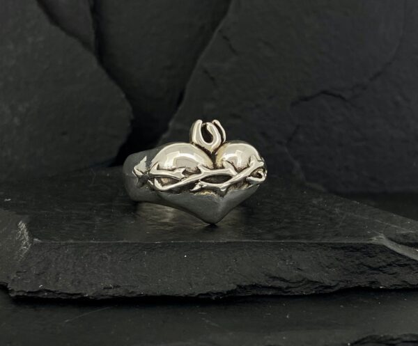 Silver ring with a heart and Om symbol on a dark stone background.