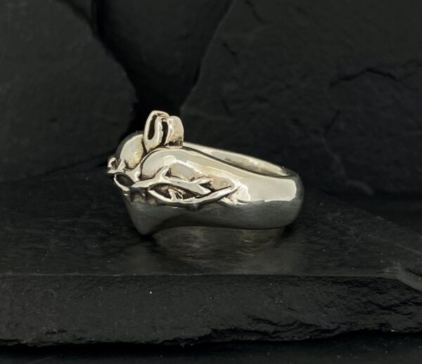 A silver ring with an intertwined design on a black textured surface.