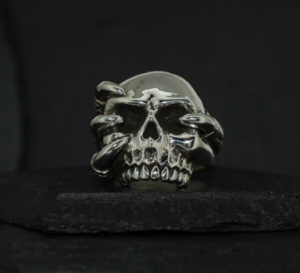 Metal skull ring with intricate serpent design on dark background.