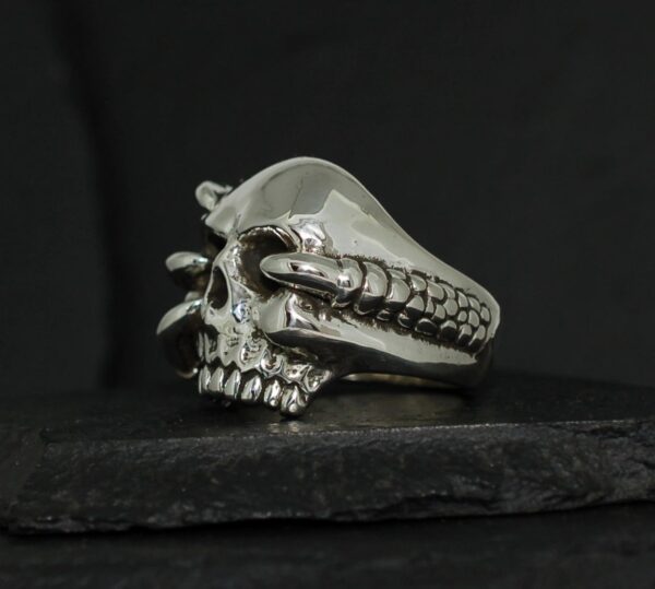 A silver skull ring with detailed teeth and eye sockets on a black background.