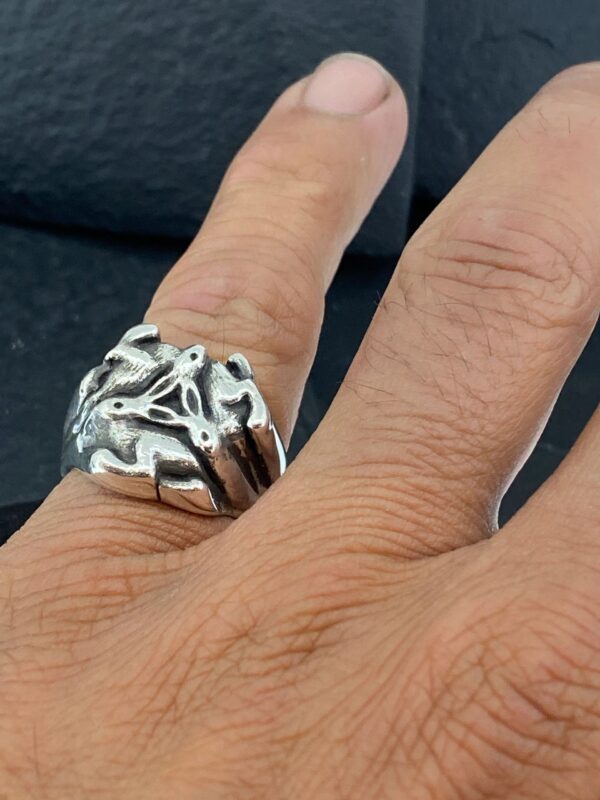 Silver ring with intricate design worn on finger.
