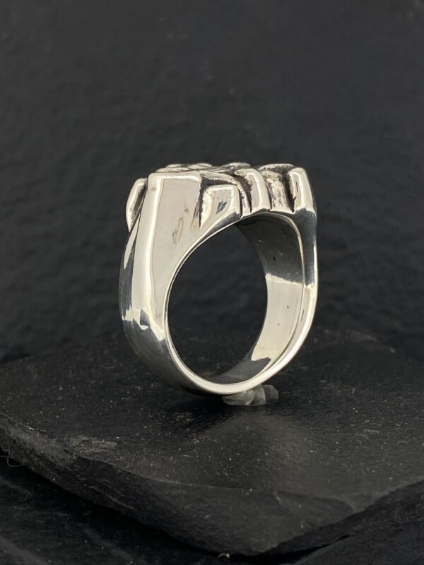 Silver ring with a bold, geometric design on a dark surface.