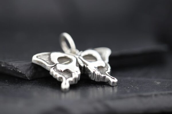 Close-up of a silver butterfly pendant on a dark surface.