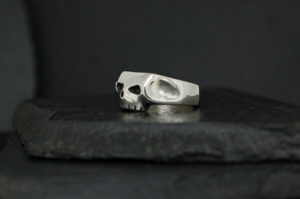 A silver ring featuring a skull design on a dark surface.