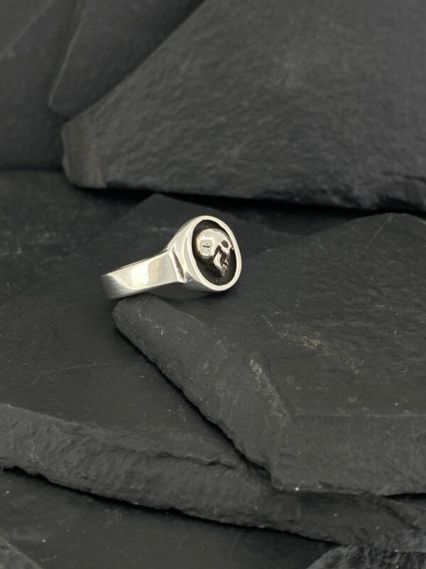 Silver ring with a black skull emblem on slate stones.