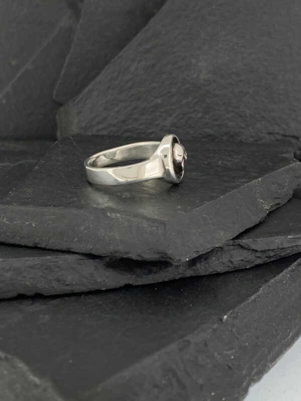 Elegant silver ring with a central gemstone on dark slate tiles.