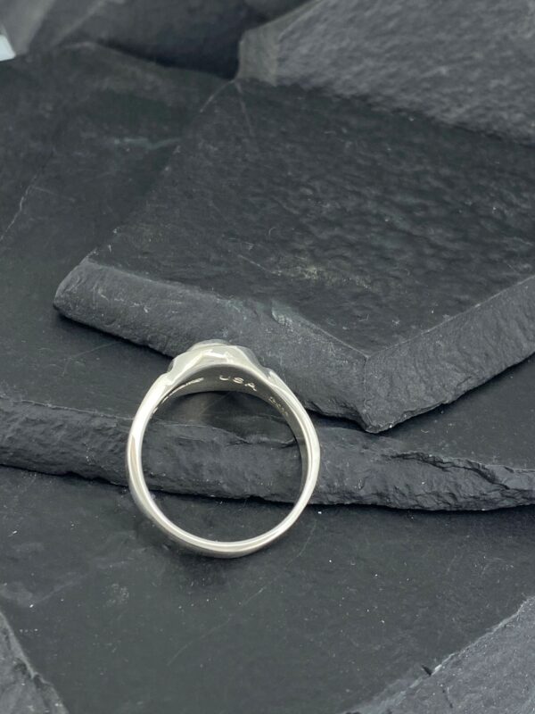 Elegant silver ring with a smooth design on a dark textured surface.