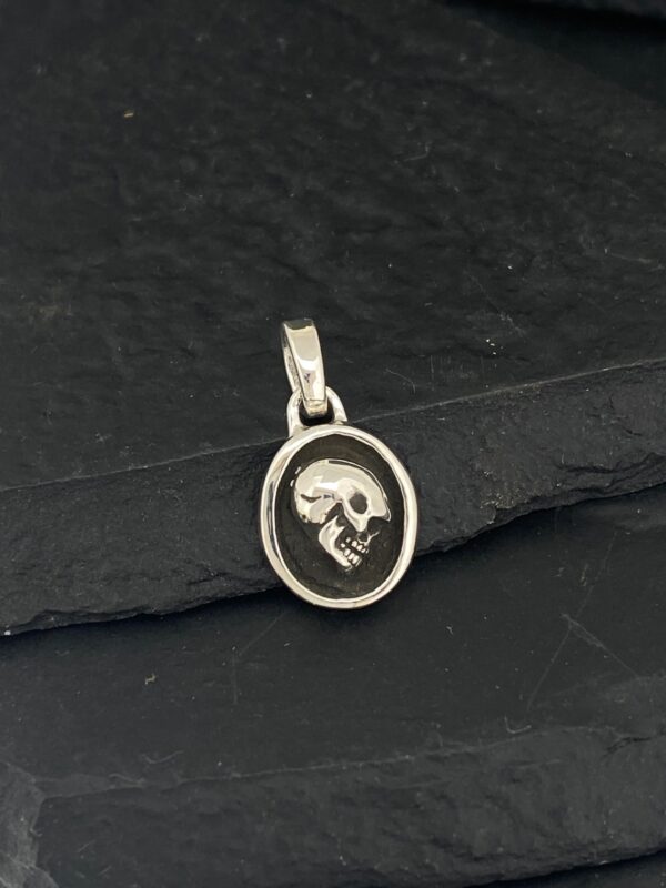 Oval silver pendant featuring a detailed skull design.