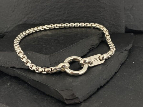 Elegant silver bracelet with a circular clasp on a dark textured surface.