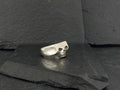 A silver skull ring on a dark textured surface.