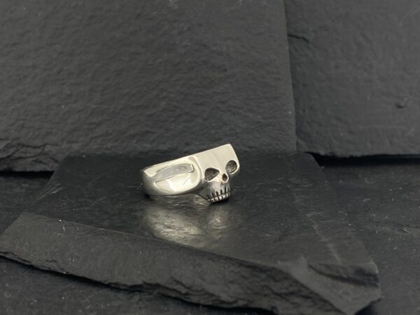 A silver skull ring on a dark textured surface.
