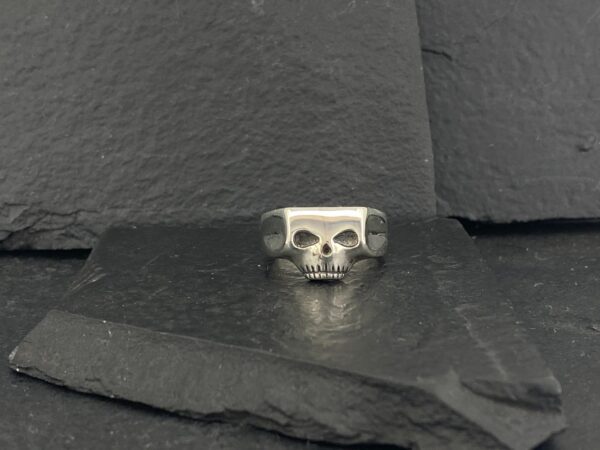 Silver skull ring on a dark stone surface.