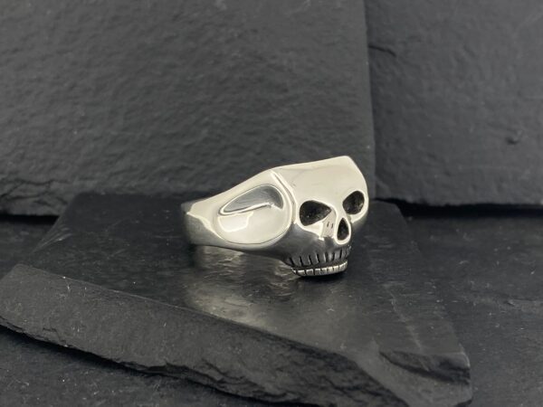 A silver skull ring resting on dark slate stones.