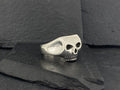 A silver skull ring resting on dark slate stones.