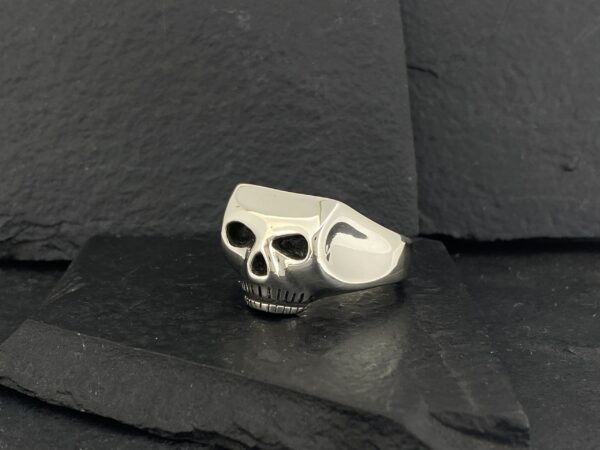 A silver skull-shaped ring on a dark surface.